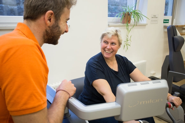 Eine Frau auf dem Ergometer mit dem Therapeuten an ihrer Seite